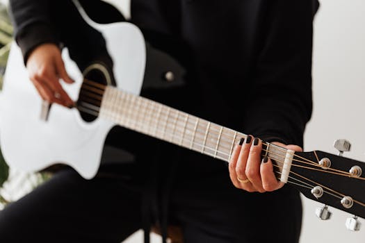 A woman strums an acoustic guitar indoors, focusing on the strings and fingers.