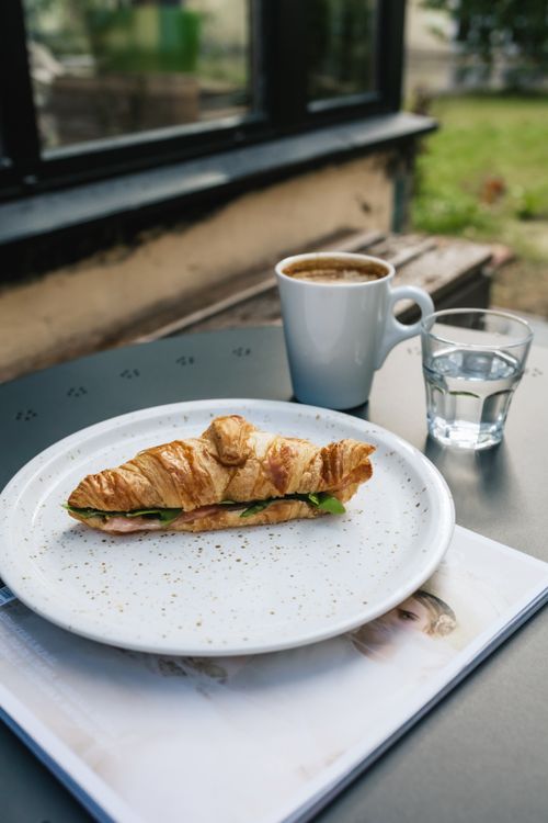 Free Savor a fresh croissant sandwich with coffee in a serene outdoor setting. Stock Photo