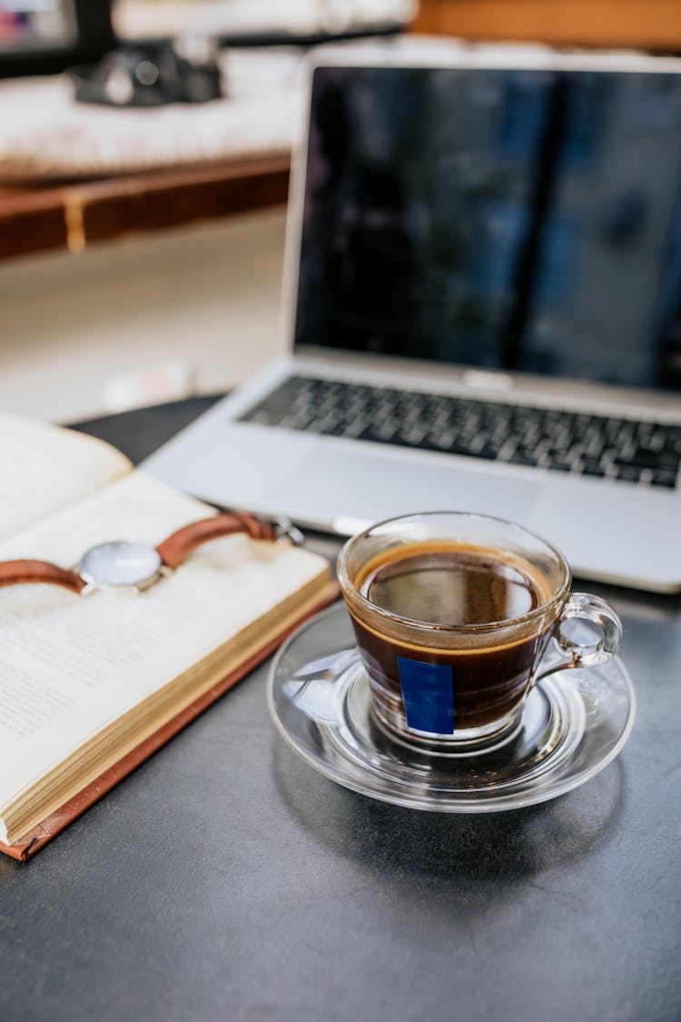 Close-Up Photo Of A Black Coffee Near A Book And Laptop