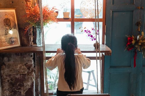 Free Back view anonymous little girl in white casual shirt playing on swings near windowsill in shabby weathered room in daylight Stock Photo