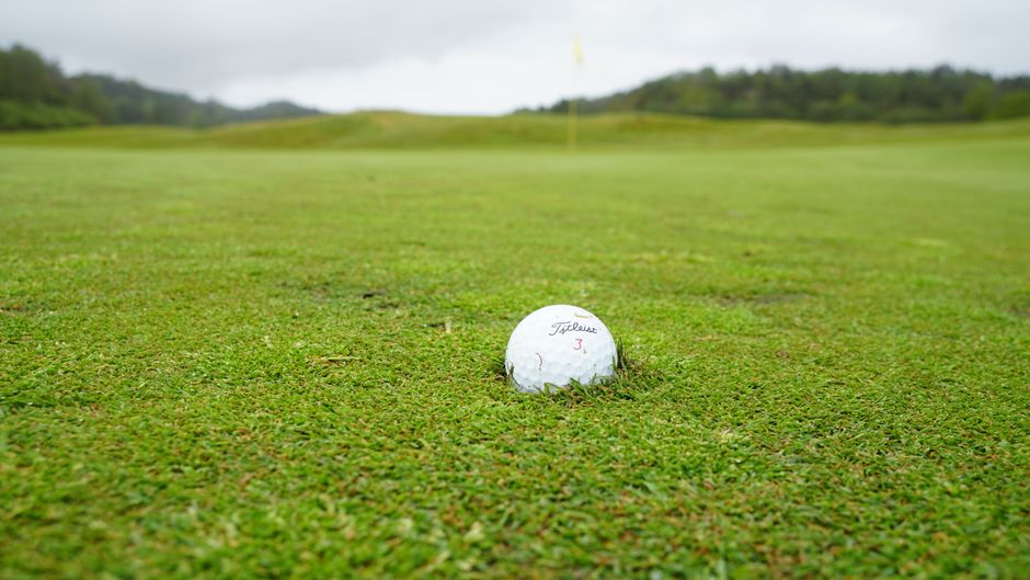 Close-up of a golf ball on a lush green golf course with cloudy skies in the background.