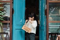 Photo of Girl Holding Wooden Welcome Signage While Standing on Doorway