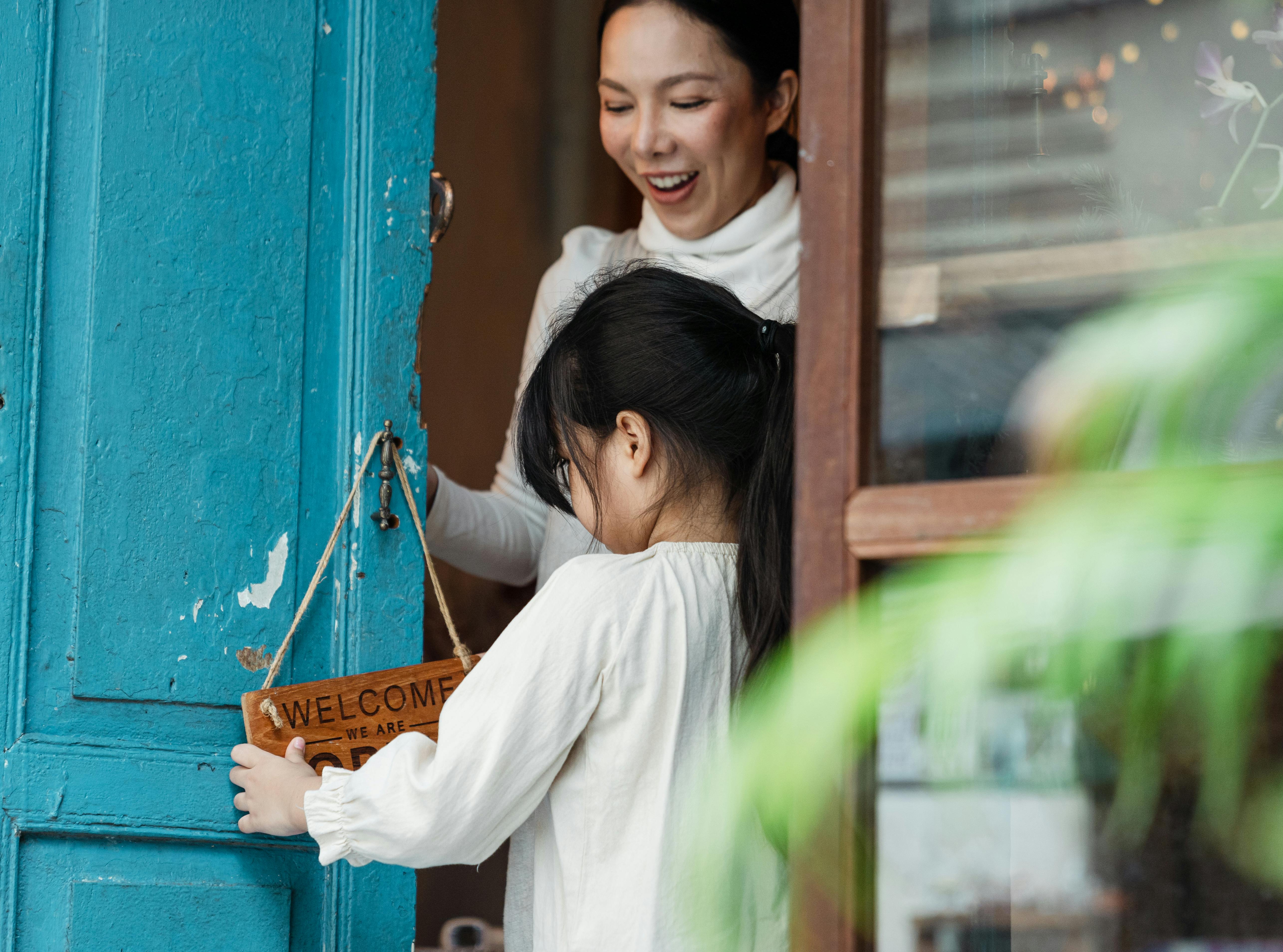 photo of girl holding wooden signage while standing near woman smiling