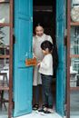 Full body happy Asian woman with cute daughter hanging open sign on shabby rural cafe door on daytime