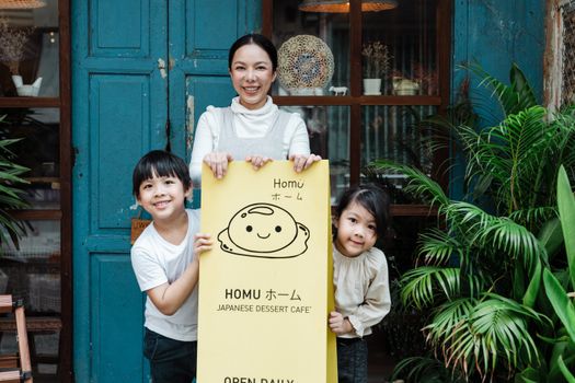 一位母亲和孩子开心地微笑着，在一家日本甜点咖啡馆外举着牌子