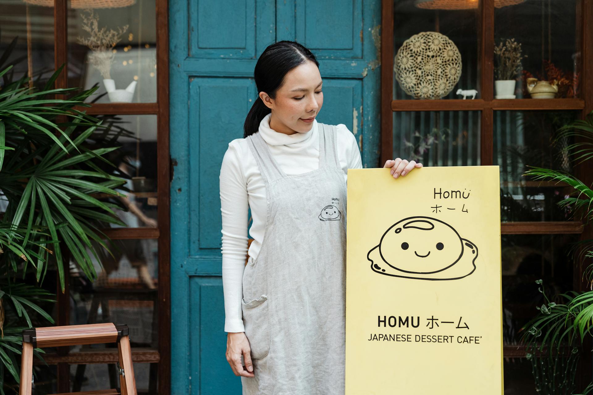 Woman displaying a sign for a Japanese dessert café outside a blue door.