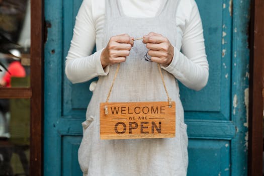 A person holds a "Welcome, we are open" sign in front of a rustic blue door.