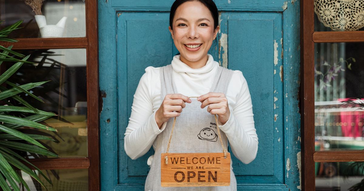 Pemilik kafe tersenyum menunjukkan papan buka usaha baru dengan modal kecil