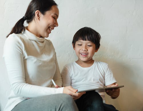 Crop ethnic mother browsing tablet with glad child