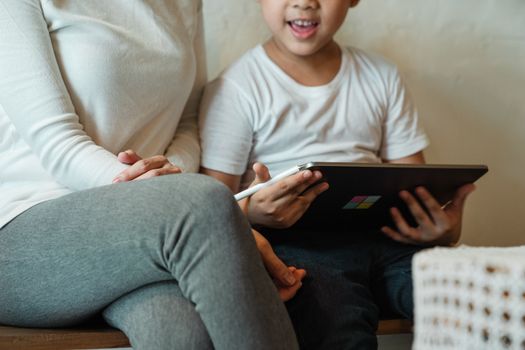 A child using a tablet at home, sitting beside their parent.