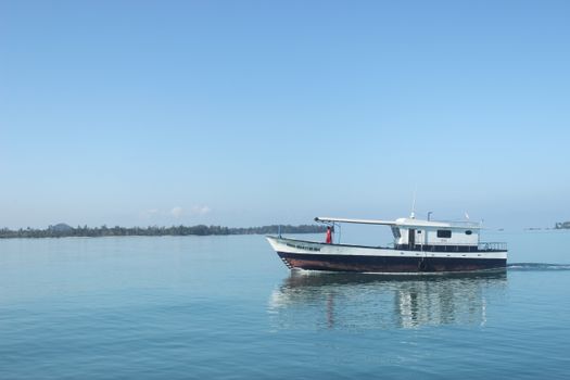 A lone motorboat navigates calm Indonesian waters under a clear blue sky.