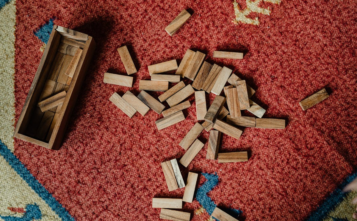 Top view of wooden box and pile of blocks for playing in jenga tower game arranged on floor carpet