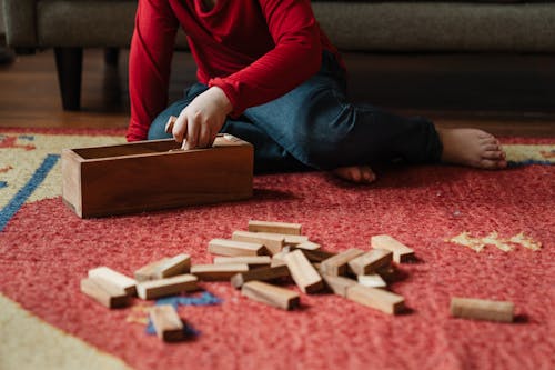 Unrecognizable barefoot kid playing jenga at home