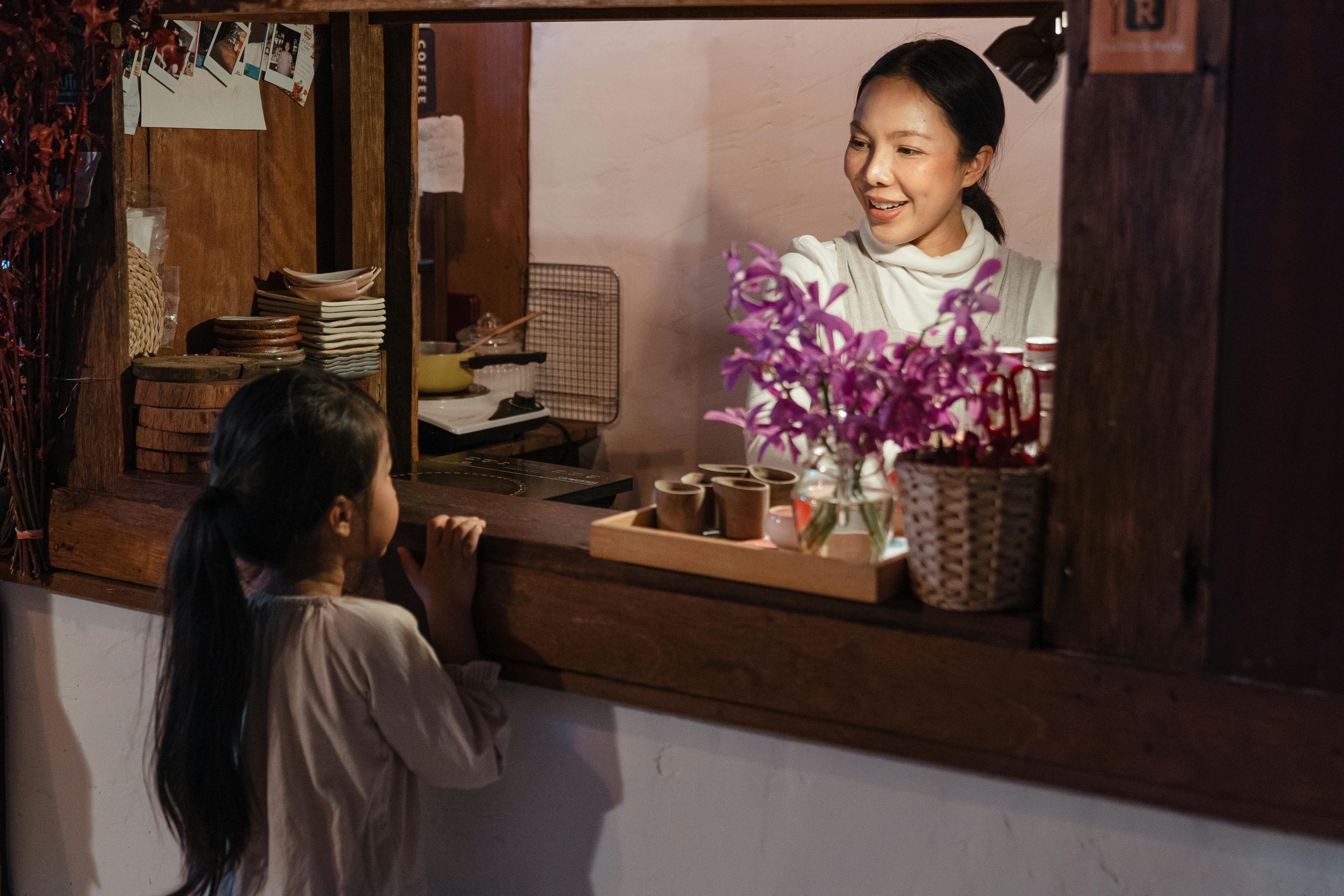 cheerful adult ethnic female worker talking with cute girl in cafe