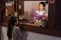 在摆满鲜花和杯子的乡村咖啡馆柜台里，一位快乐的女士和孩子正在互动