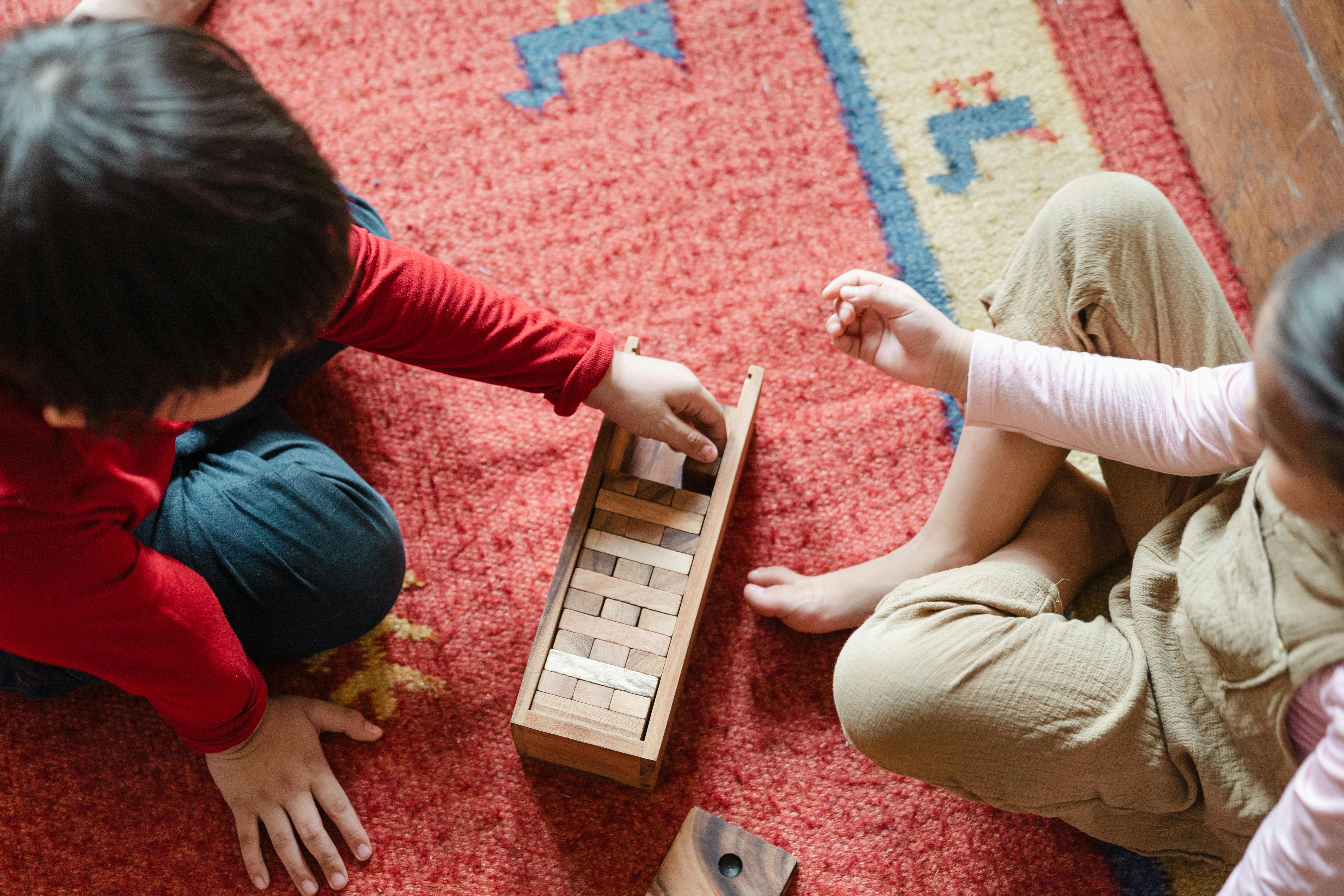 crop cute kids playing jenga on floor at home