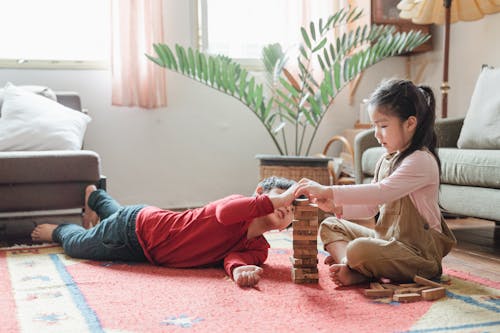 Adorable Asian kids building wooden tower on floor at home
