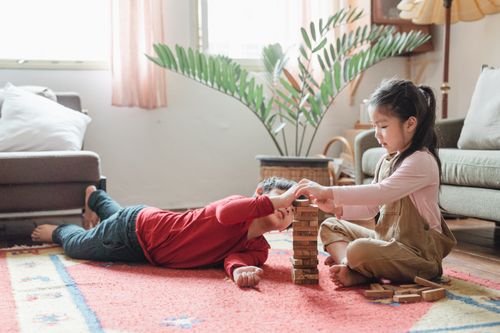 Free Content barefoot ethnic boy and girl playing jenga block game together on floor carpet between cozy sofas in modern room interior Stock Photo