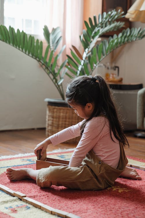 Cute barefoot Asian girl playing jenga on floor