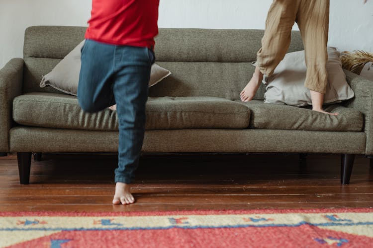 Crop Children Jumping On Sofa At Home