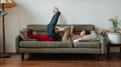 Free Full body barefoot Asian brother and sister lying on cozy sofa while spending free time in modern living room during weekend Stock Photo