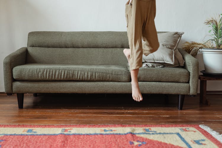 Crop Girl Jumping From Sofa At Home