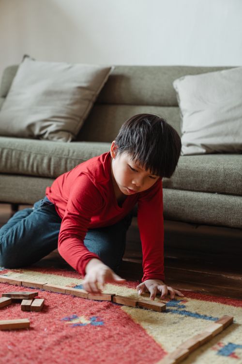 Free Young boy playing with wooden blocks on a colorful carpet in a cozy living room. Stock Photo