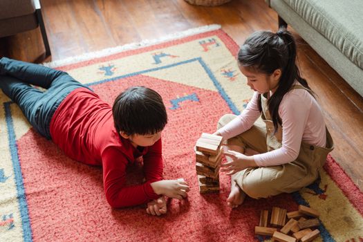 Two kids enjoying playtime with wooden blocks on a colorful rug indoors.