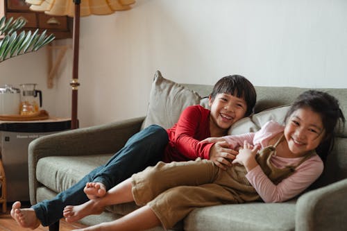 灰色のソファに座って楽しんでいる2人の子供の写真