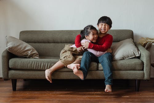 Free Photo of Two Kids Sitting on Gray Couch While Hugging Each Other Stock Photo