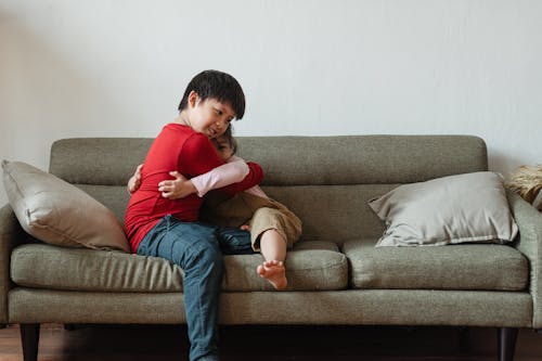 Photo of Two Kids Hugging Each Other While Sitting on Gray Sofa