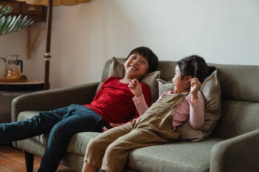 两个孩子坐在温暖客厅的沙发上，微笑着享受休闲时光