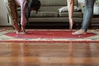 清晨，在现代化客厅里，一位年轻的少数族裔妇女和可爱的小女孩正一起在地毯上做伸展运动，沙发旁舒适地铺着地毯