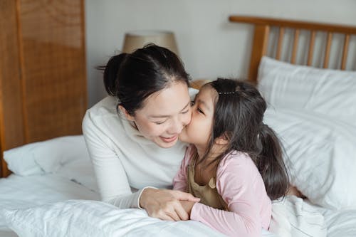 Free Happy ethnic woman resting on bed with adorable daughter Stock Photo