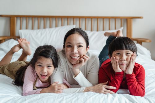 Free Full length happy ethnic mother and daughter and son in casual clothes lying on stomachs on soft bed in daylight Stock Photo