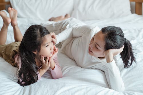 Photo of Woman and Girl Talking While Lying on Bed