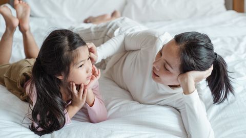 A mother and daughter bonding indoors, lying on a bed and enjoying quality time together.