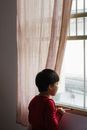 室内，一个年幼的孩子挂着透明窗帘，若有所思地看着窗外