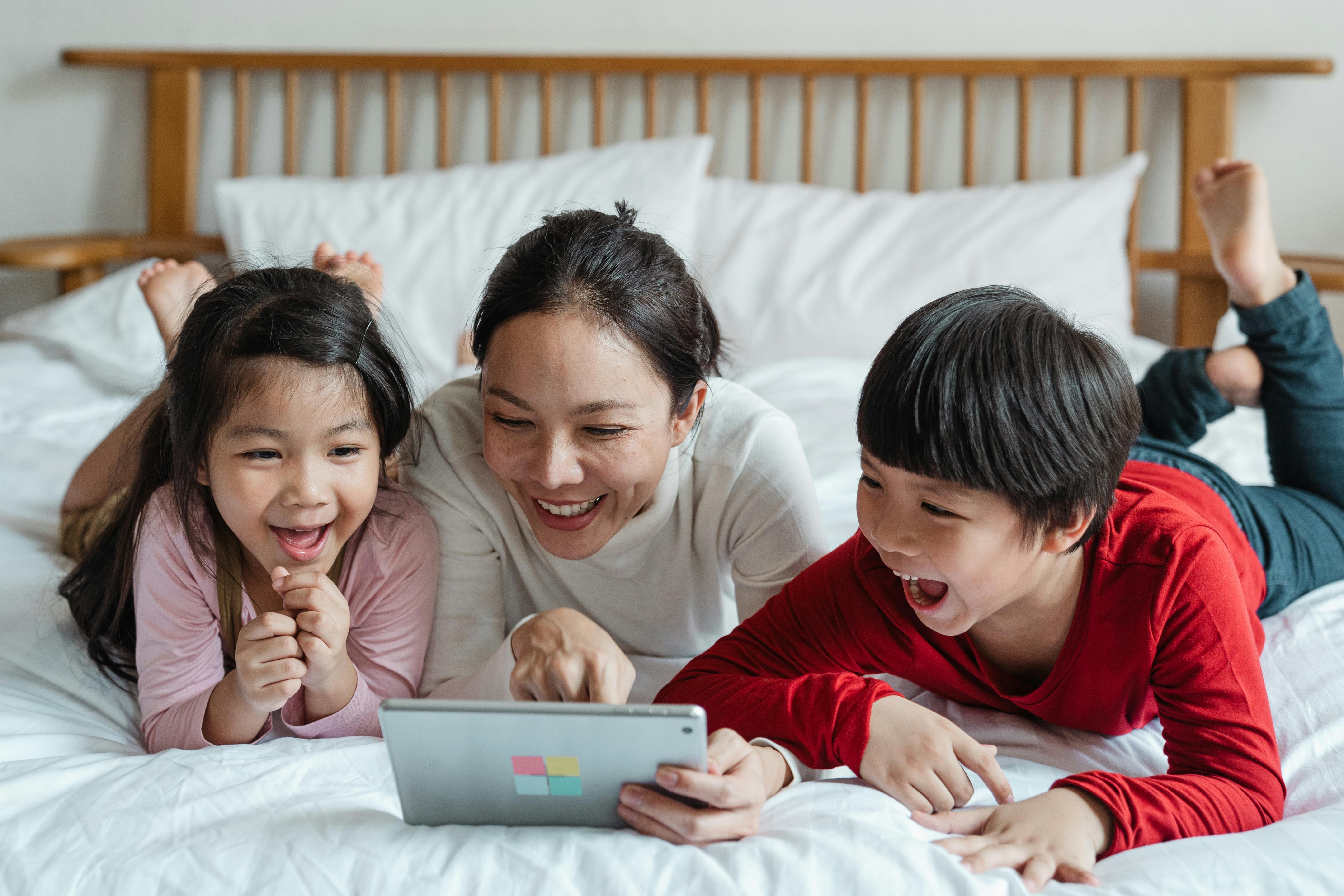 cheerful ethnic mother pointing at tablet screen and children watching and laughing