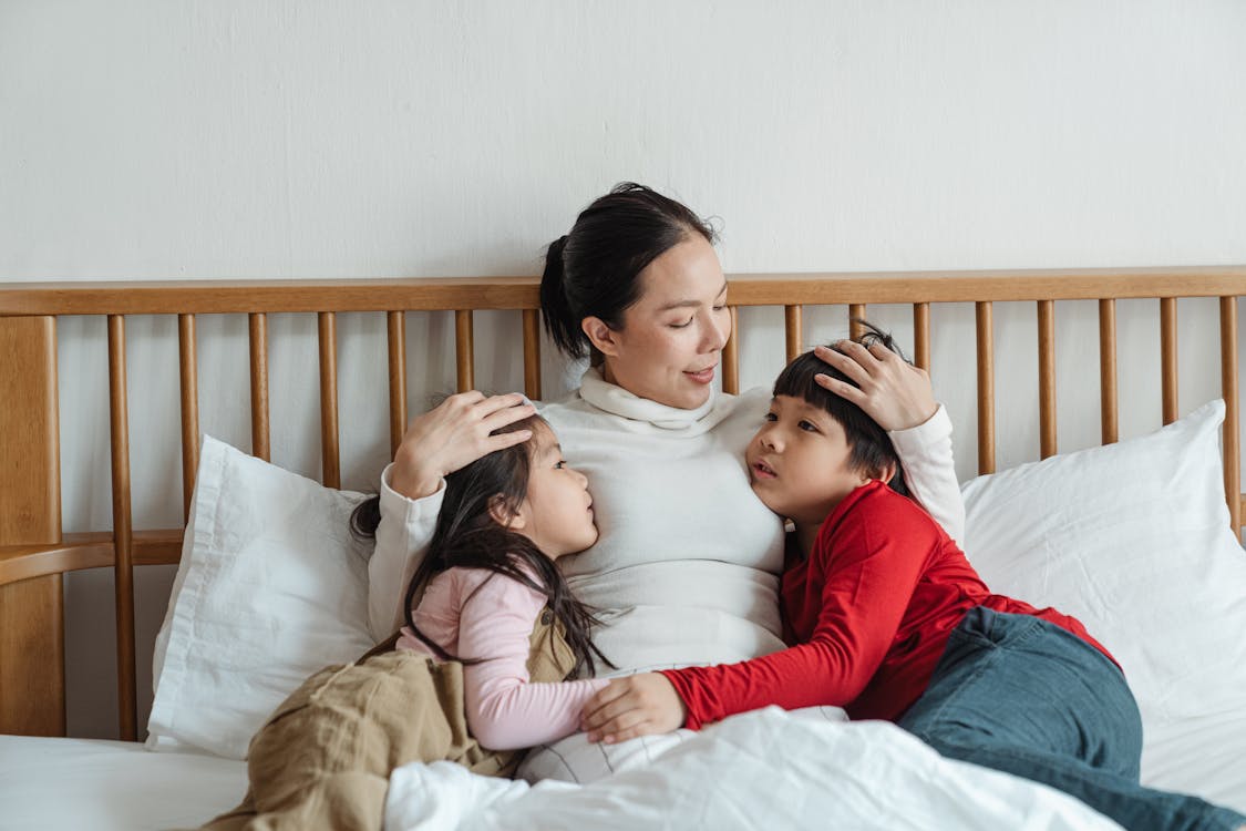 Calm Asian little children hugging mother while woman patting kids on heads