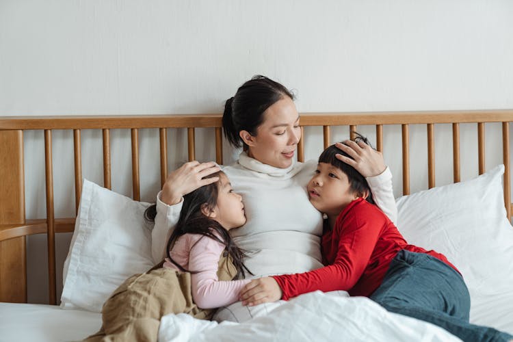 Calm Asian Little Children Hugging Mother While Woman Patting Kids On Heads