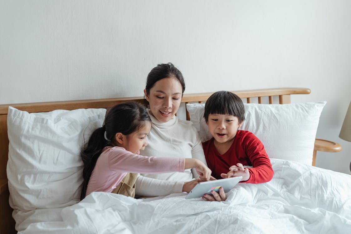 Free Photo of Woman and Kids Sitting on Bed While Using Tablet Computer Stock Photo