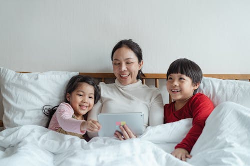 Positive ethnic mother and little children using tablet in bed