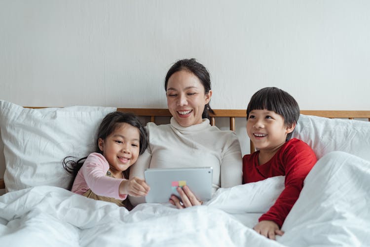 Positive Ethnic Mother And Little Children Using Tablet In Bed