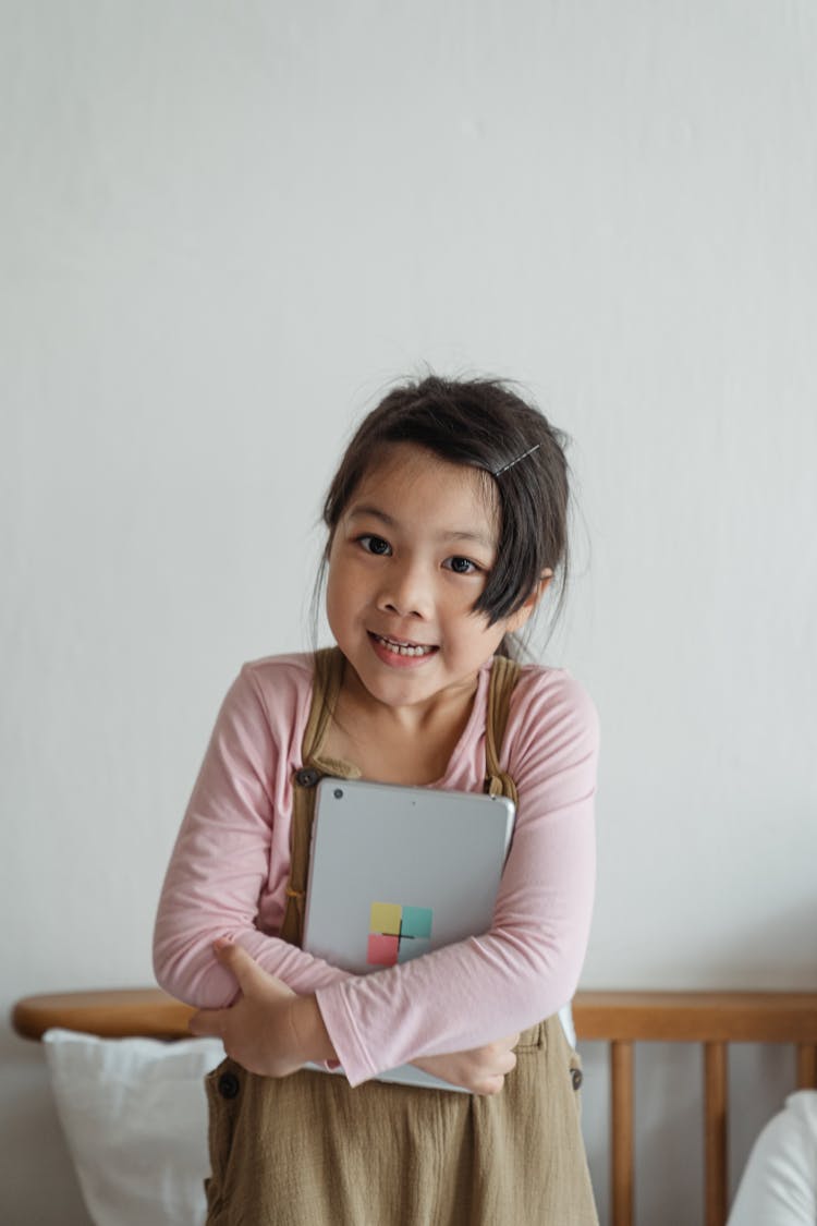 Smiling Asian Girl Cuddling Tablet To Chest