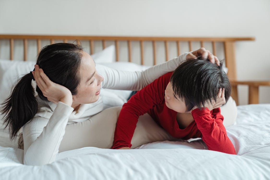Free Caring mother patting little son on head on bed Stock Photo