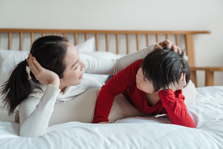 Caring Mother Patting Little Son On Head On Bed