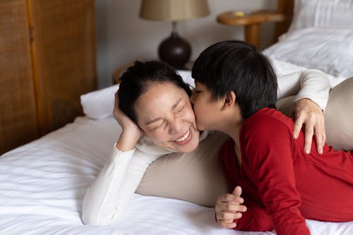 Little boy kissing squinting mother on bed