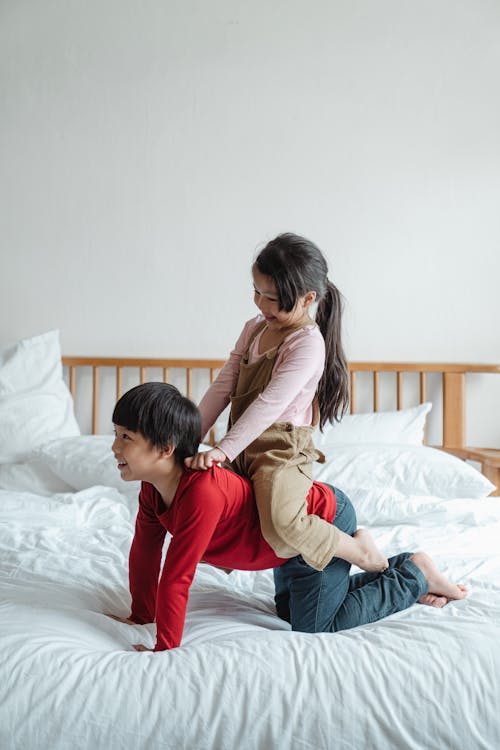 Positive ethnic brother giving piggyback ride to sister on bed