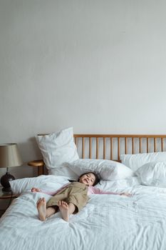 年轻的女孩躺在床上，身下是舒适的白色床单，她微笑着享受这室内的轻松时刻